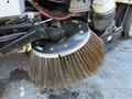 A close-up of a sweeping attachment mounted on a 2016 Isuzu NPR featuring long bristles designed for street cleaning