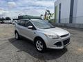 A silver 2015 Ford Escape parked on gravel with a sleek design featuring a front grille and modern headlights