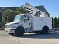 A 2006 Freightliner M2 106 bucket truck with a white body and a raised aerial lift on top parked on the street