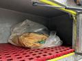 A large brown bag wrapped in plastic is resting on a red plastic shelf inside a storage compartment of a Freightliner FLL086 truck