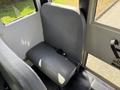 A grey upholstered passenger seat inside a 2011 Freightliner B2 bus with a safety seatbelt attached