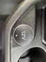 A black circular button labeled 12V on a textured surface in a vehicle interior