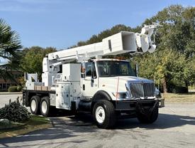 A white 2006 International 7500 truck with an extended hydraulic boom and an equipment bed is parked on a paved area