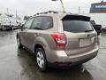 A 2016 Subaru Forester in a muted beige color with a compact SUV design and roof rails, showing rear and side profiles with distinctive taillights and alloy wheels