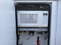 A white microwave oven is placed inside a compartment with several shelves and a metal bracket holding objects underneath