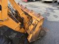 A close-up of the front shovel bucket of a 2005 Case 570 featuring hydraulic lines and a weathered orange paint finish