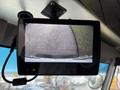 A display screen showing a rearview camera feed of a parking area with visible pavement and grass edges
