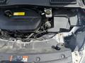 The engine compartment of a 2015 Ford Escape displaying the engine cover various components and labels