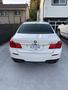 A white 2011 BMW 7-Series viewed from the rear with a visible license plate and distinctive tail lights