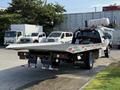 A 2022 Ford F600 flatbed truck with a silver exterior is parked, featuring a long flatbed and various lights on the rear section