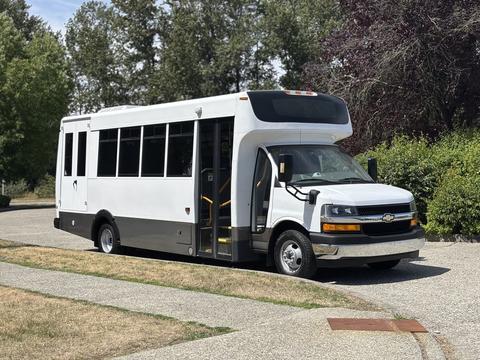 A 2020 Chevrolet Express shuttle bus with a white body and black lower section is parked with the side door open showcasing steps and handrails