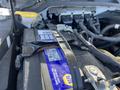 A close-up of a car battery labeled with a yellow and blue NAPA logo secured with a metal strap in a vehicle engine compartment