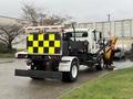 A 2016 Freightliner 108SD truck in white with a yellow and black checkerboard pattern on the back and an attached snowplow blade