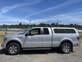 A silver 2014 Ford F-150 with a gray truck bed cover parked on gravel showcasing its large tires and chrome accents