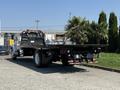 A 2008 Ford F-750 flatbed truck with a black body and red taillights parked with palm trees on the flatbed