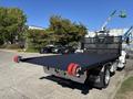 A 2020 Peterbilt 330 flatbed truck with a black bed and red rollers at the rear is positioned for transport with a sturdy metal railing on the sides