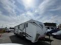 A 2013 Outdoor Wind River travel trailer with a white exterior and decorative gray and brown accents parked in a lot