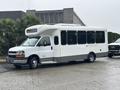 A 2018 Chevrolet Express shuttle bus with a white exterior and large windows parked on a wet surface