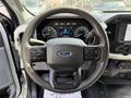 Steering wheel of a 2021 Ford F-150 featuring control buttons on either side and a digital display behind the wheel showing speedometer and other gauges