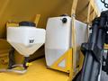 A white plastic tank labeled NSF connected to a hose next to a larger white tank with a spout attached to a yellow truck body