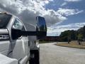 A 2016 Ford F-750 truck with a prominent side mirror and white exterior parked on a paved area with a view of the road ahead