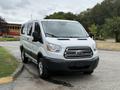 A white 2017 Ford Transit T150 XLT van with a large front grille and sliding side door parked at an angle facing forward
