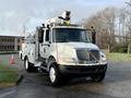A 2013 International Durastar 4300 utility truck equipped with a raised aerial boom and tool compartments on the side