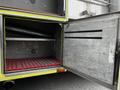 An open storage compartment of a 1995 Freightliner FLL086 featuring metal shelving and a red grided mat on the bottom
