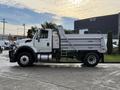 A 2011 International WorkStar truck with a white body and silver dump bed parked on a surface with visible tire tracks
