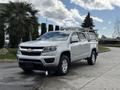 A 2018 Chevrolet Colorado pickup truck with a silver exterior parked on the road featuring a ladder rack on its bed and a Chevrolet logo on the front grille