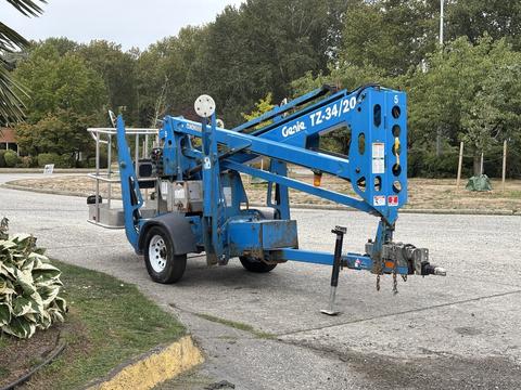 A blue 2016 Genie TZ-34/20 articulated boom lift with a basket attachment and trailer hitch parked on a concrete surface