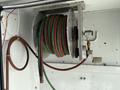 A metal hose reel mounted on a wall with a green and red hose coiled around it and a brass connector attached to the end of the hose