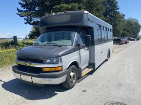 A 2016 Chevrolet Express bus in a gray and black color scheme with a large windshield and side steps for entry