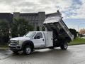 A white 2012 Ford F-550 dump truck with its bed raised, showcasing the cargo area designed for transporting materials