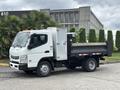 A 2015 Mitsubishi Fuso FE160 with a white cab and a black dump bed parked on a paved surface