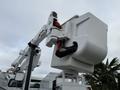 A white utility bucket truck with an extended aerial lift arm and a bucket attachment on a clear day