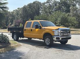A 2013 Ford F-250 Super Duty pickup truck in bright yellow with a flatbed attached parked on a street