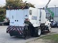A 2012 International DuraStar 4300 street sweeper with a white body and black bristles at the front for cleaning streets and parking lots