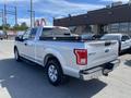 A silver 2015 Ford F-150 parked with a black tool box in the truck bed and a clean exterior showing clear reflections and a well-maintained look