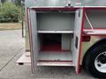 Open compartment of a 2002 GMC C7500 with metal shelves and a textured floor mat inside