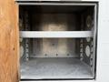 An open metal storage compartment with a wooden door and a single horizontal metal shelf inside