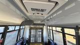 Interior view of a 2021 Ford Transit showing a white ceiling with an emergency exit sign and a wheelchair ramp at the entrance with two blue seats visible