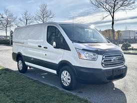 A 2017 Ford Transit van in white with a black lower section parked on a street featuring a high roof and large cargo area