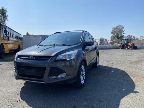 A 2016 Ford Escape in a dark color with a sleek design parked in a gravel area showing its front and side profile