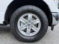 A close-up view of a silver alloy wheel on a 2021 Ford F-150 featuring a large all-terrain tire with an aggressive tread pattern and the Ford logo on the center cap