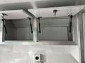 Two upper storage cabinets with metal hinges and gas struts, mounted against a metallic wall, designed for utility storage in a vehicle