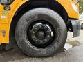 A close-up view of a black wheel from a yellow 2014 Freightliner B2 school bus showcasing the tire tread and shiny hubcap