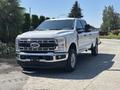 A 2023 Ford F-350 Super Duty truck in silver with a chrome front grille and large tires is parked in a driveway