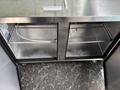 A stainless steel commercial refrigerator with two open sections featuring wire shelves inside each compartment