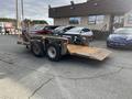 A 2013 JLG Industries Flat Deck Trailer with a steel frame and two wheels is shown in the foreground with a lowered ramp for loading items